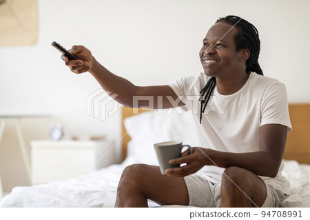 Smiling Black Man Drinking Coffee And Watching TV While Relaxing At Home 94708991