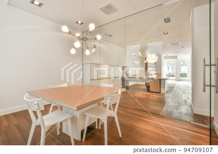 Table with chairs and flowers located near lounge area and kitchen in spacious room of contemporary apartment Table with chairs and flowers located near lounge area and kitchen in spacious room of contemporary apartment 94709107