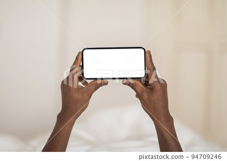 Mobile Mockup. Unrecognizable Black Man Holding Blank Smartphone While Lying In Bed Mobile Mockup. Unrecognizable Black Man Holding Blank Smartphone While Lying In Bed 94709246
