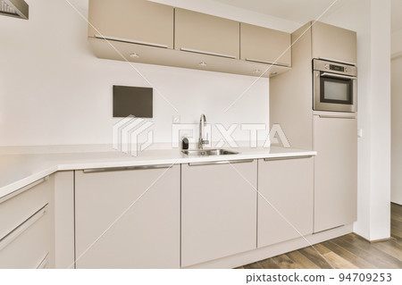 Fragment of interior of light narrow home kitchen with minimalist style white furniture with sink and stove Fragment of interior of light narrow home kitchen with minimalist style white furniture with sink and stove 94709253