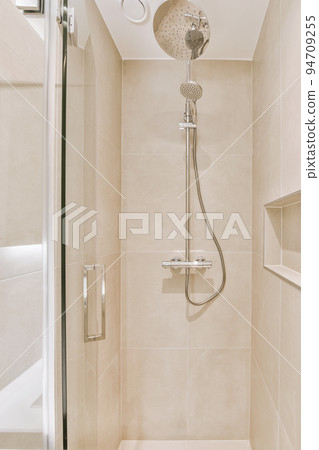 Shower faucets attached to tiled wall near glass partition and ornamental curtail in washroom at home Shower faucets attached to tiled wall near glass partition and ornamental curtail in washroom at home 94709255