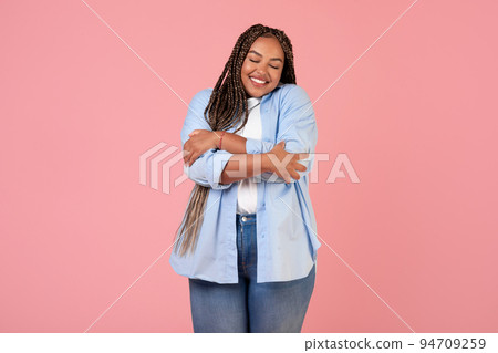 Happy African American Overweight Female Hugging Herself Over Pink Background Happy African American Overweight Female Hugging Herself Over Pink Background 94709259