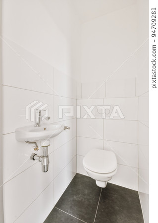 Interior of narrow restroom with sink and wall hung toilet with white walls and checkered floor Interior of narrow restroom with sink and wall hung toilet with white walls and checkered floor 94709281