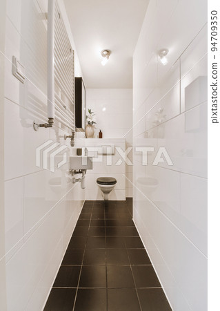 Interior of narrow restroom with sink and wall hung toilet with white walls and checkered floor 94709350