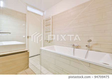 Sinks with mirrors and clean bathtub located near shower box with glass door in modern bathroom with white tiled walls Sinks with mirrors and clean bathtub located near shower box with glass door in modern bathroom with white tiled walls 94709475
