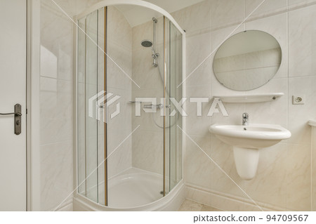 Sinks with mirrors and clean bathtub located near shower box with glass door in modern bathroom with white tiled walls Sinks with mirrors and clean bathtub located near shower box with glass door in modern bathroom with white tiled walls 94709567