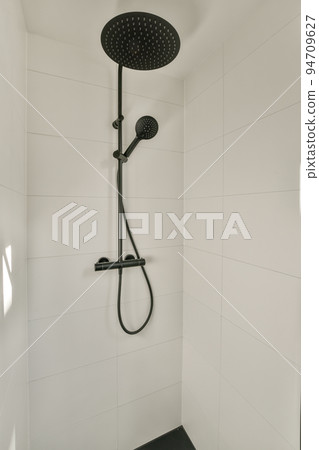 Shower faucets attached to tiled wall near glass partition and ornamental curtail in washroom at home Shower faucets attached to tiled wall near glass partition and ornamental curtail in washroom at home 94709627