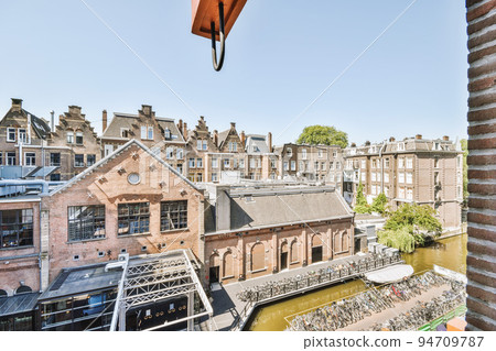 Panoramic view of old brick buildings with parking and trees from small balcony Panoramic view of old brick buildings with parking and trees from small balcony 94709787