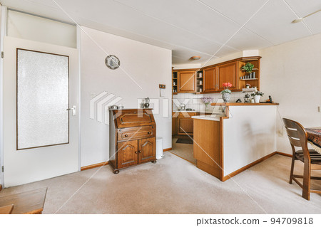 Contemporary minimalist style interior design of light studio apartment with wooden table and chairs in dining zone between open kitchen and living room with white walls and parquet floor 94709818