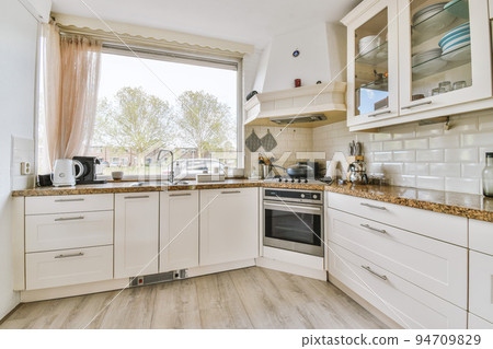 Fragment of interior of light narrow home kitchen with minimalist style white furniture with sink and stove 94709829