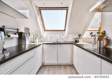 Fragment of interior of light narrow home kitchen with minimalist style white furniture with sink and stove Fragment of interior of light narrow home kitchen with minimalist style white furniture with sink and stove 94709893