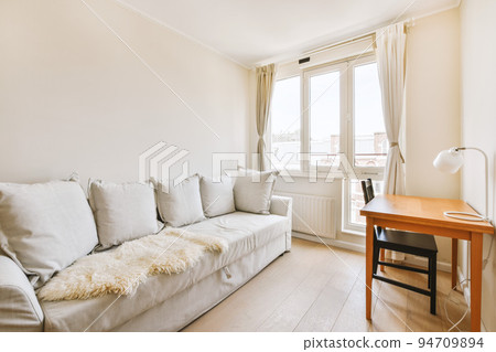 Comfortable couch located near carpet and table against window in spacious minimalist style living room in modern apartment Comfortable couch located near carpet and table against window in spacious minimalist style living room in modern apartment 94709894