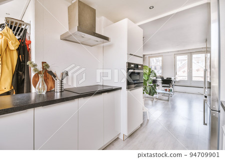 Fragment of interior of light narrow home kitchen with minimalist style white furniture with sink and stove Fragment of interior of light narrow home kitchen with minimalist style white furniture with sink and stove 94709901