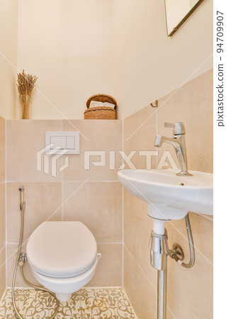 Interior of narrow restroom with sink and wall hung toilet with white walls and checkered floor Interior of narrow restroom with sink and wall hung toilet with white walls and checkered floor 94709907
