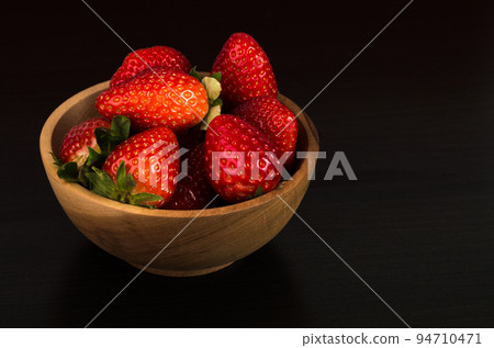 Fresh red strawberries in a wooden bowl on dark wooden background Fresh red strawberries in a wooden bowl on dark wooden background 94710471