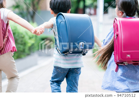 Elementary school students holding hands and walking on the sidewalk 94710512