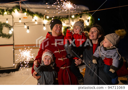 Happy family celebrates christmas in nature and holds sparklers. Parents with three sons travels in a van. Happy family celebrates christmas in nature and holds sparklers. Parents with three sons travels in a van. 94711069