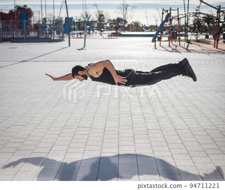 A man in black sportswear jumps doing push-ups in the park. 94711221