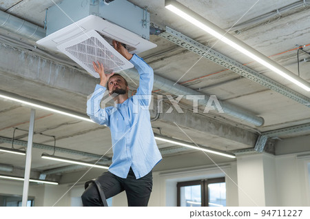 Caucasian bearded man repairing the air conditioner in the office.  94711227