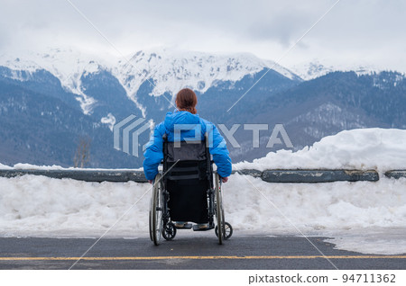 Rear view of a woman in a wheelchair travels in the mountains in winter. Rear view of a woman in a wheelchair travels in the mountains in winter. 94711362