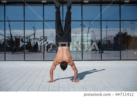 A man doing a handstand outdoors against of panoramic windows.  94711412