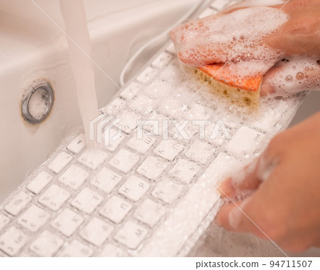 Woman washing white computer keyboard with a sponge with foam. Woman washing white computer keyboard with a sponge with foam. 94711507