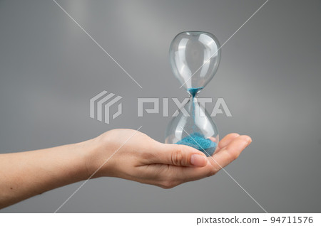 Woman holding an hourglass on a gray background. Close-up. 94711576