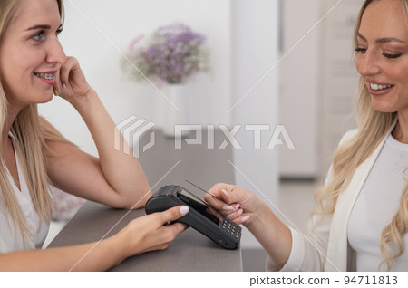 A young woman pays in a beauty salon with a credit card using NFC contactless payment.  94711813
