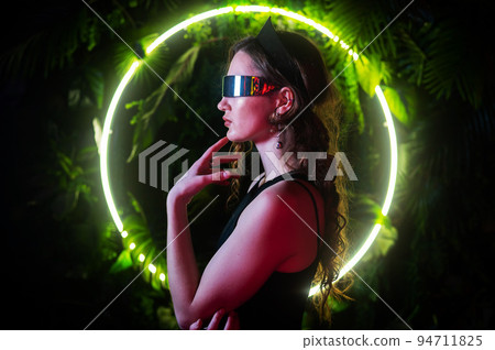 Caucasian woman in panoramic sunglasses against the background of an annular neon lamp in plants.  94711825