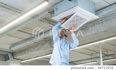 Caucasian bearded man repairing the air conditioner in the office. Caucasian bearded man repairing the air conditioner in the office. 94711916
