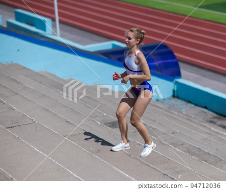 Young caucasian woman running on stadium stairs outdoors.  94712036