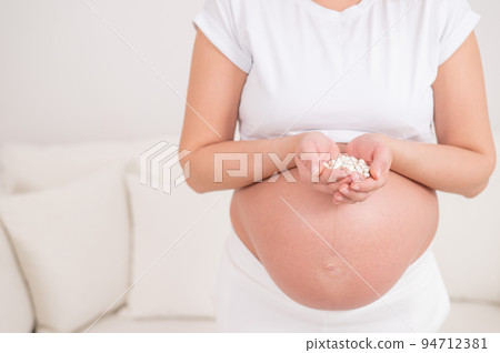 A faceless pregnant woman is holding a handful of white pills. A faceless pregnant woman is holding a handful of white pills. 94712381