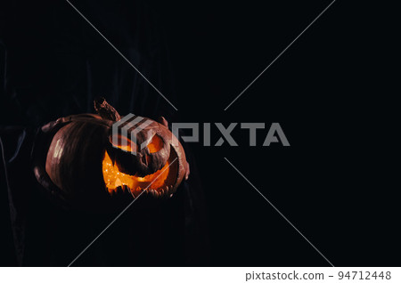 The witch is holding a pumpkin jack o lantern glowing in the dark. Halloween. 94712448