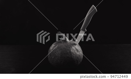 Knife in a pumpkin on a black background. Halloween symbol. Monochrome. 94712449
