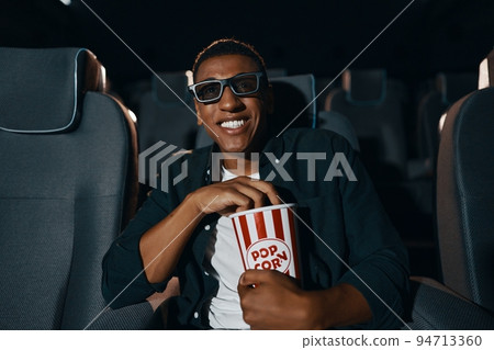 african american man in 3d glasses eating popcorn and watching film in cinema african american man in 3d glasses eating popcorn and watching film in cinema 94713360