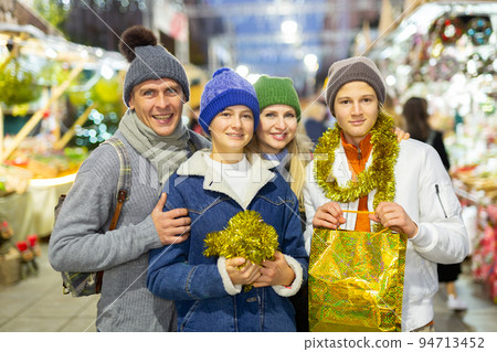 Portrait of man and woman and their happy teenagers posing with paper bags near counters at Christmas fair 94713452
