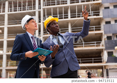 Engineers in suits and hardhats discussing on building site 94713511