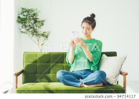Woman sitting on a sofa and looking at a smartphone Woman sitting on a sofa and looking at a smartphone 94714117