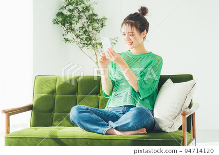 Woman sitting on a sofa and looking at a smartphone Woman sitting on a sofa and looking at a smartphone 94714120