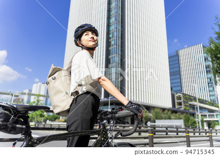 一位女商人在摩天大樓的背景下騎著背著背包的公路自行車上下班 94715345