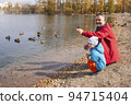 Father and son in nature in the park feeding ducks in the river in autumn 94715404