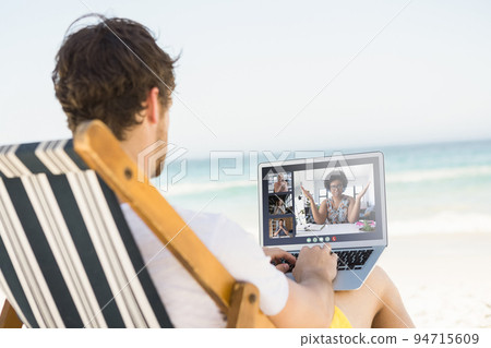 Caucasian man relaxing on beach having video call using laptop 94715609