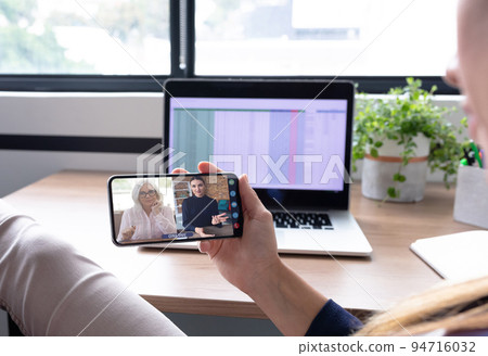 Caucasian woman using smartphone having video call with coworkers 94716032