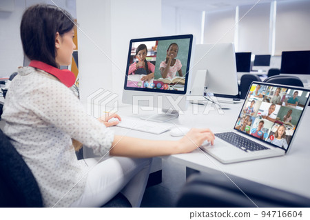 Caucasian female teacher using computer and laptop on video call with school children Caucasian female teacher using computer and laptop on video call with school children 94716604