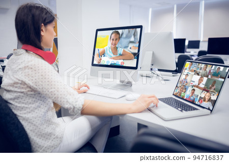 Caucasian female teacher using computer and laptop on video call with school children 94716837