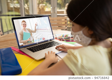 Caucasian schoolgirl wearing face mask using laptop on video call with female teacher 94716842
