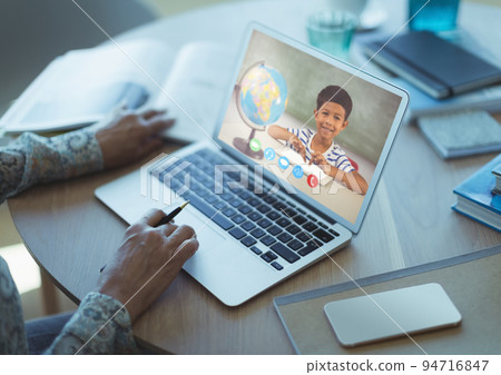 Mixed race schoolboy learning displayed on laptop screen during video call with female teacher Mixed race schoolboy learning displayed on laptop screen during video call with female teacher 94716847