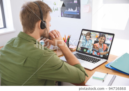 Caucasian male teacher using laptop and phone headset on video call with school children learning fr 94716868