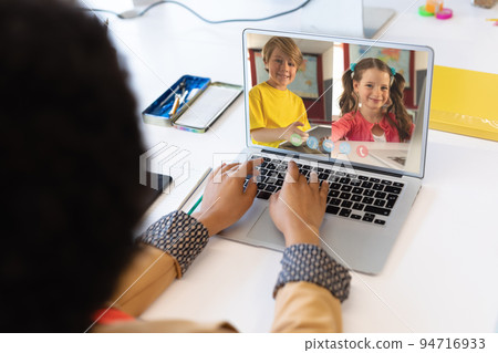Mixed race female teacher using laptop on video call with school children learning from home 94716933