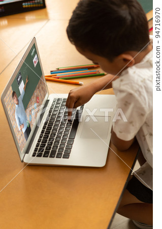 Male student having a video call with male teacher on laptop at school 94716970